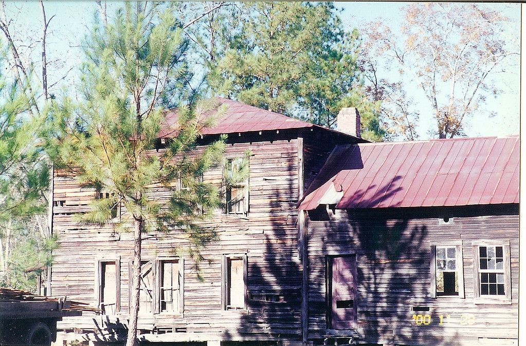 Dilapidated wooden building with a red metal roof and missing windows.