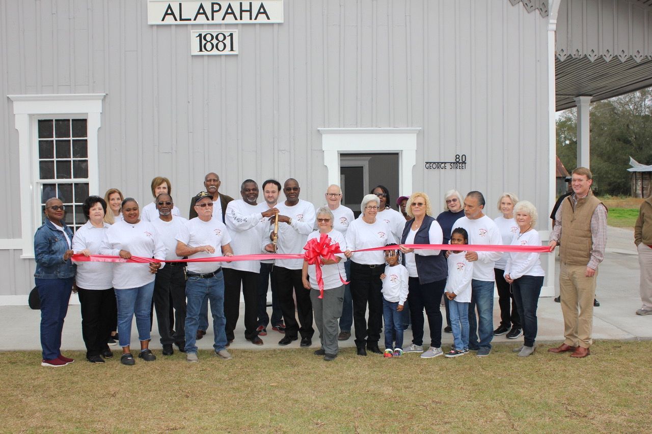 Group cuts a red ribbon in front of a gray building with