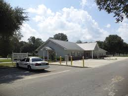Exterior view of a light blue building with a silver roof, police car parked out front on a sunny day.