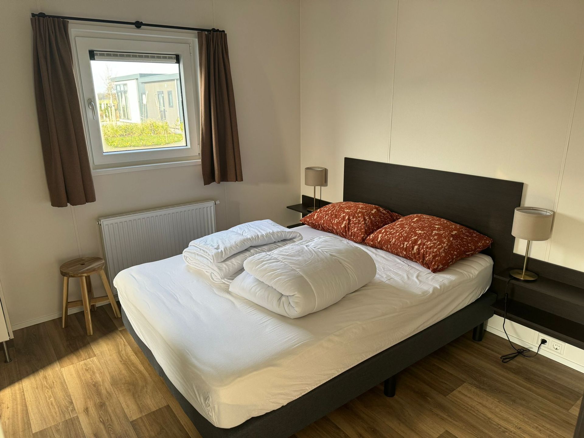 Een slaapkamer met een 2 persoons bed, twee lampen en een raam.