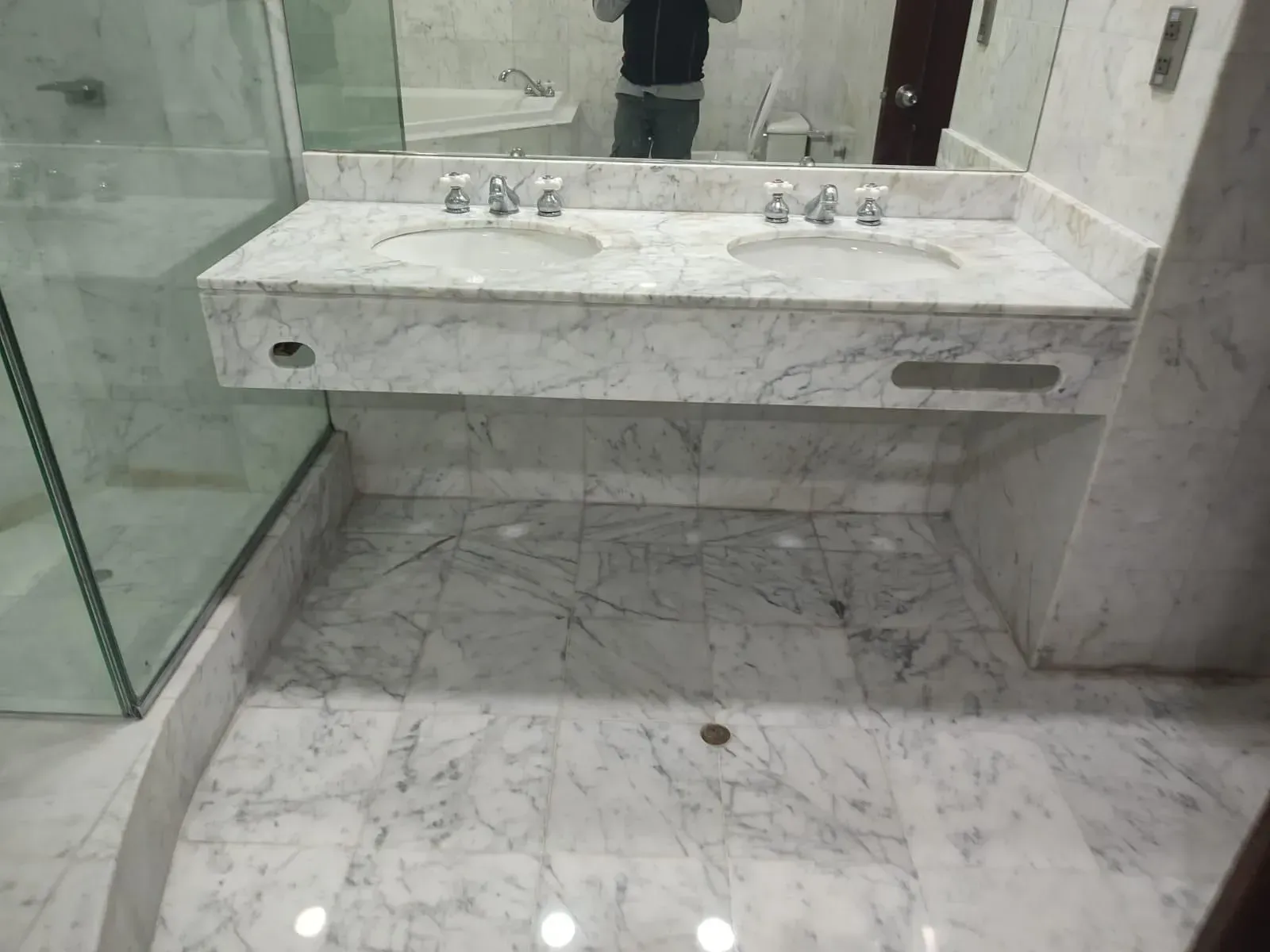 Marble bathroom with double sinks and glass shower.