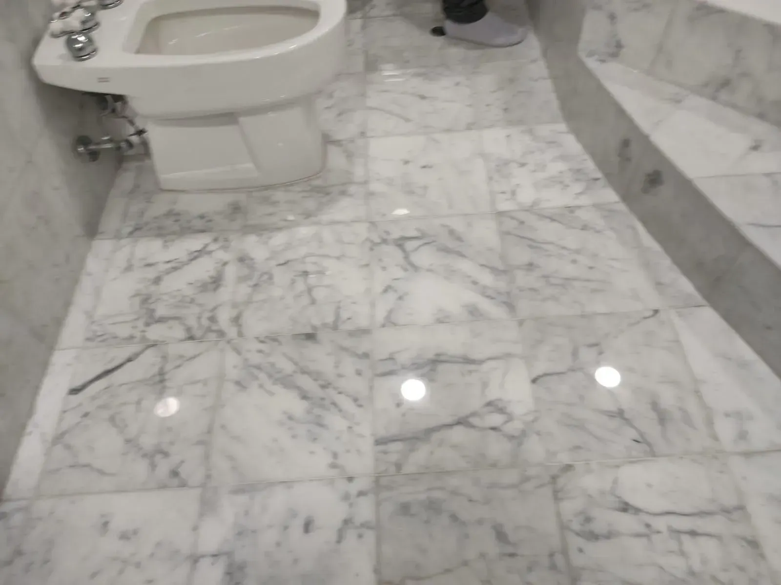 White marble tiled bathroom floor with a toilet and a bidet.
