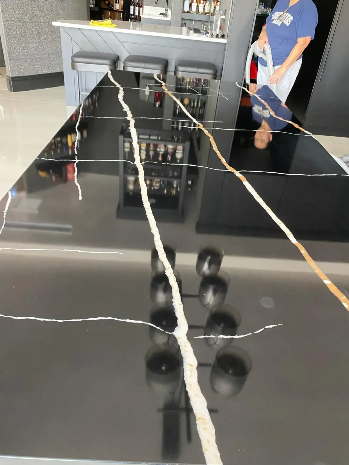 Black countertop with white and gold veining, reflecting bar and person.