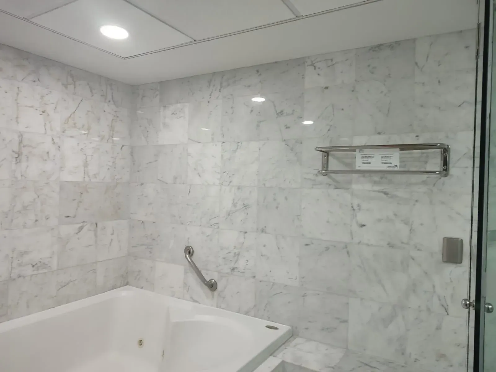 Bathroom with white marble tile, bathtub, grab bar, and towel rack.