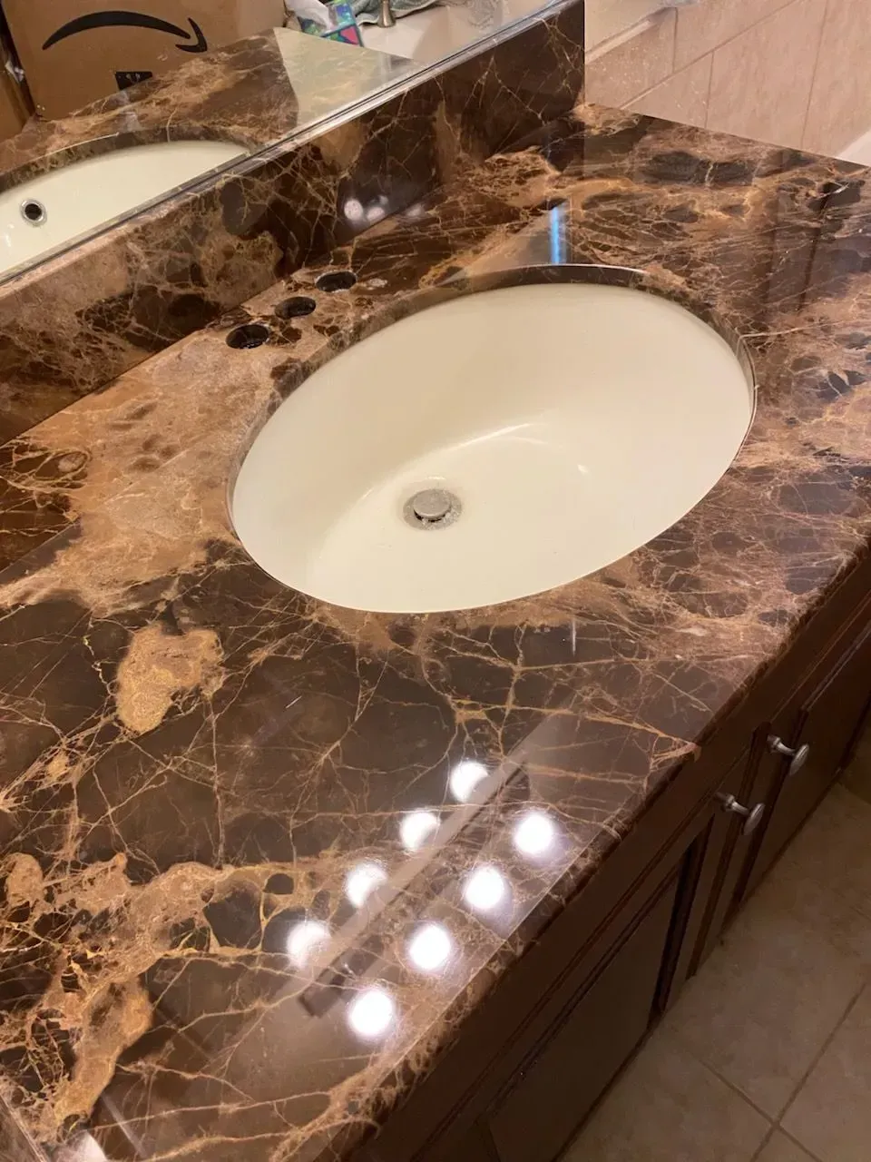 Bathroom countertop with brown and gold marble, oval sink. Wooden cabinets below.