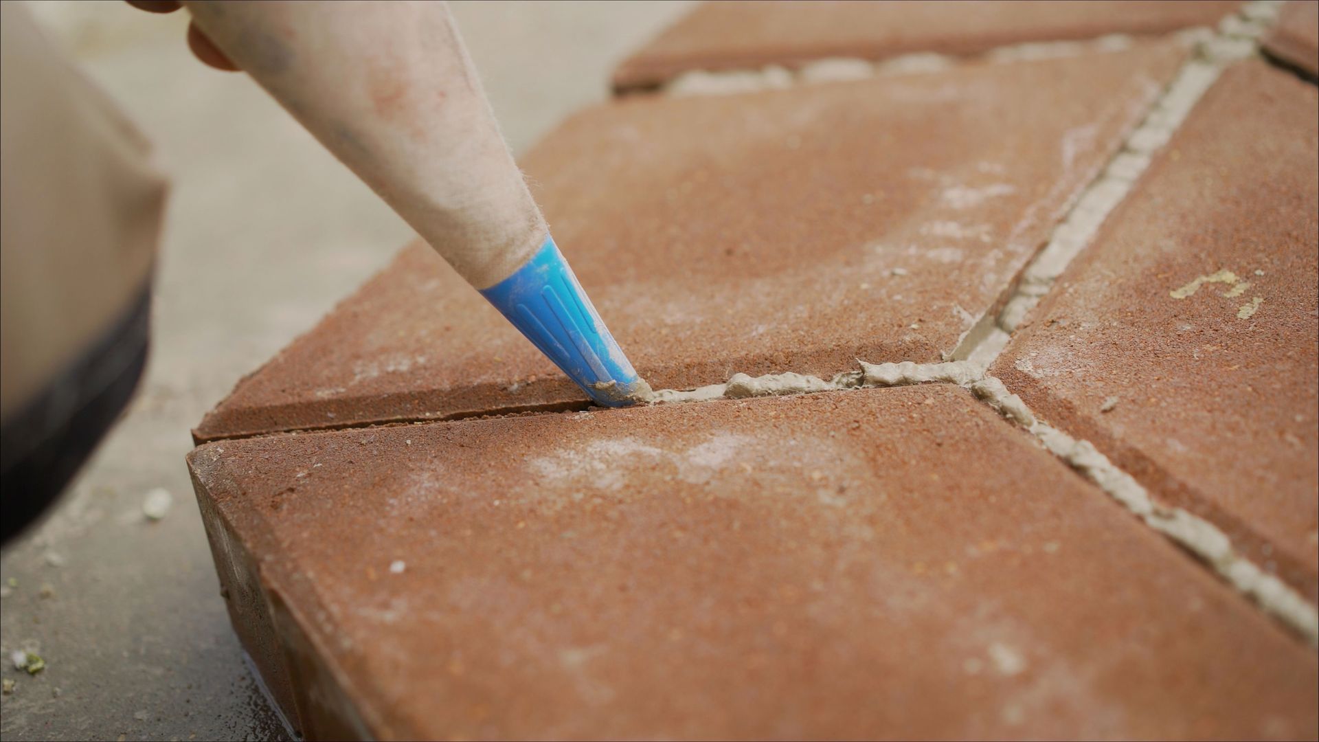 Hand filling gaps between red paving stones with a piping bag.