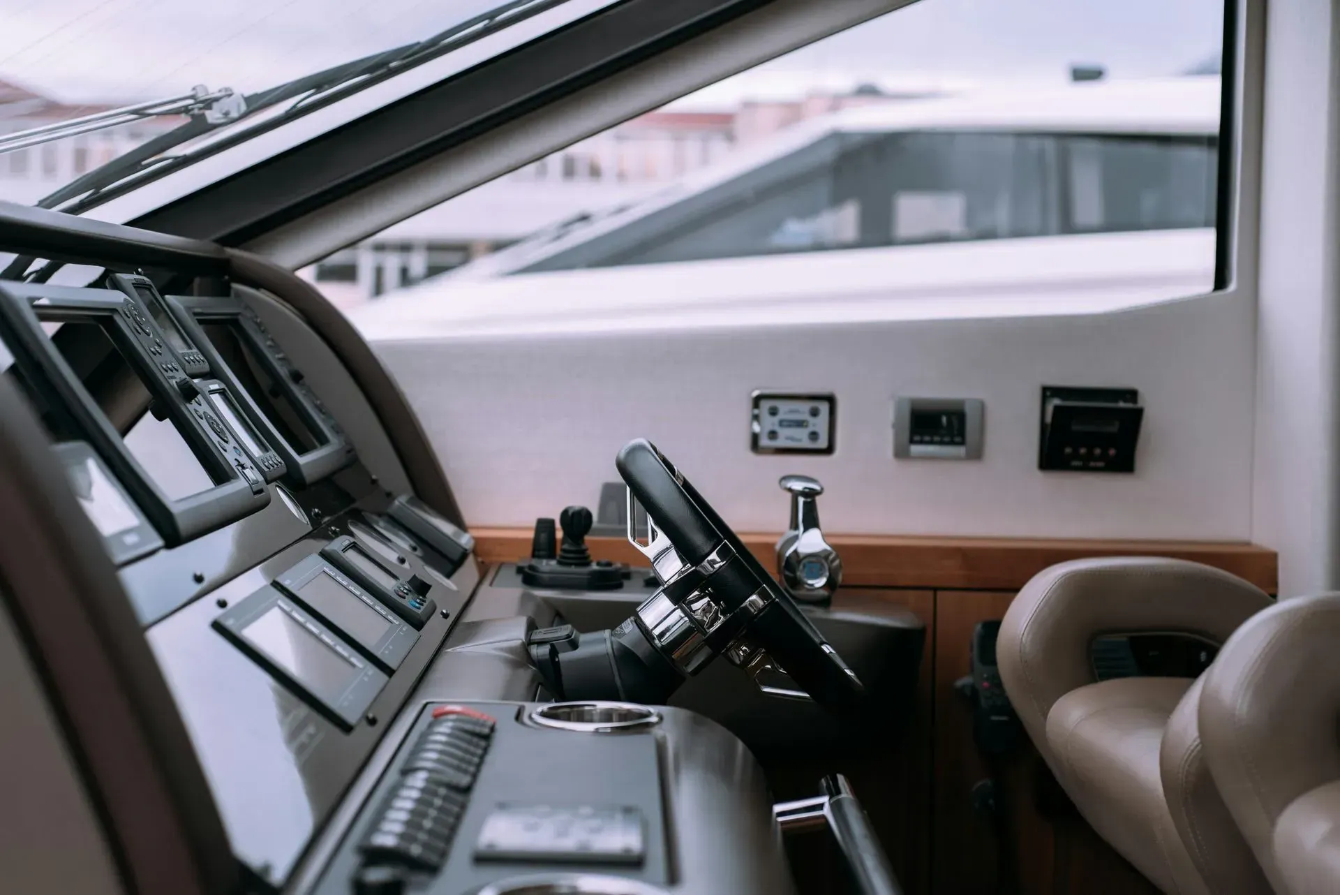Inside of a boat's cockpit, with a steering wheel and electronic controls. A view out to another boat.