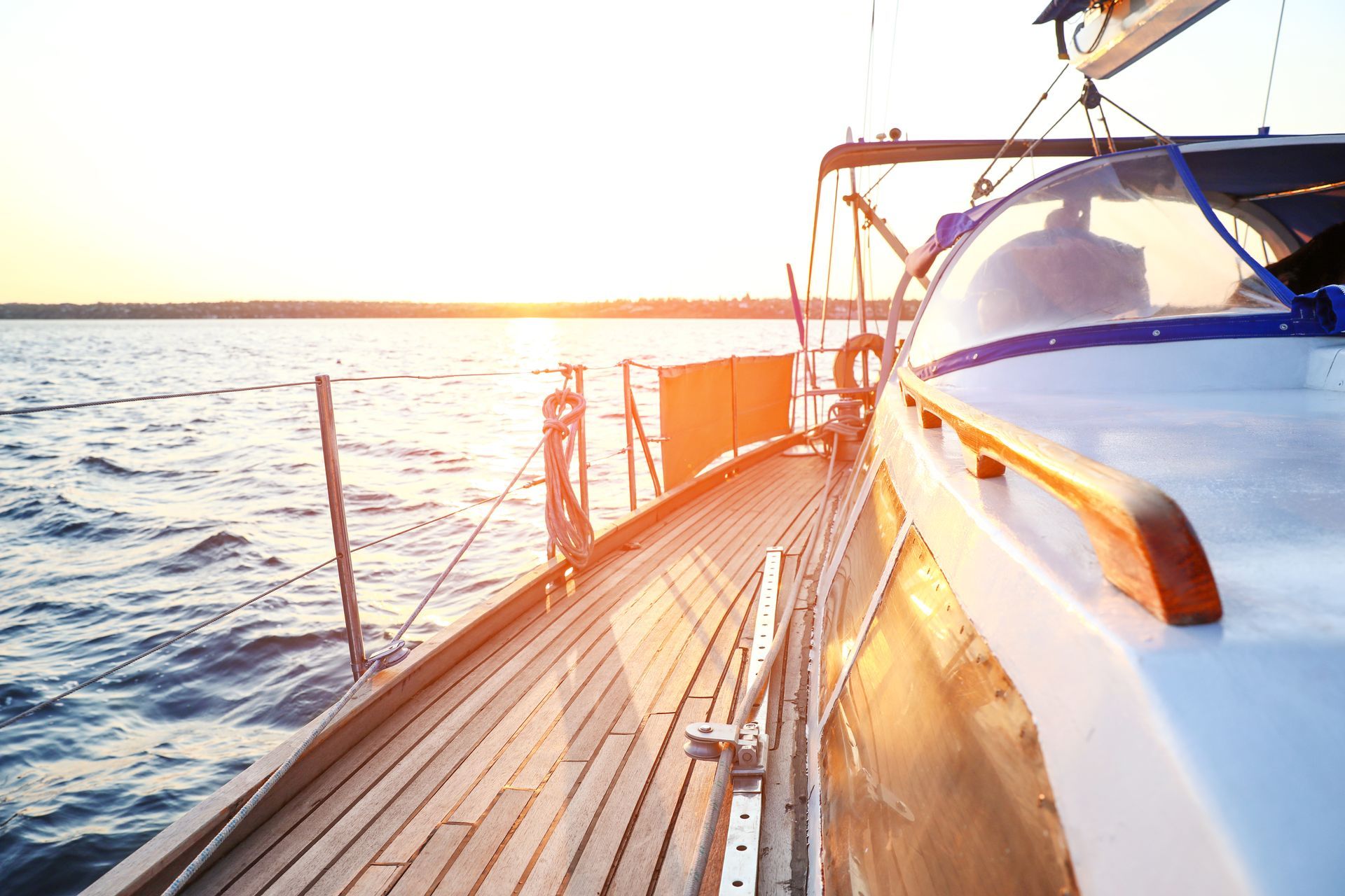 Wooden deck of a sailboat sailing on a body of water at sunset.