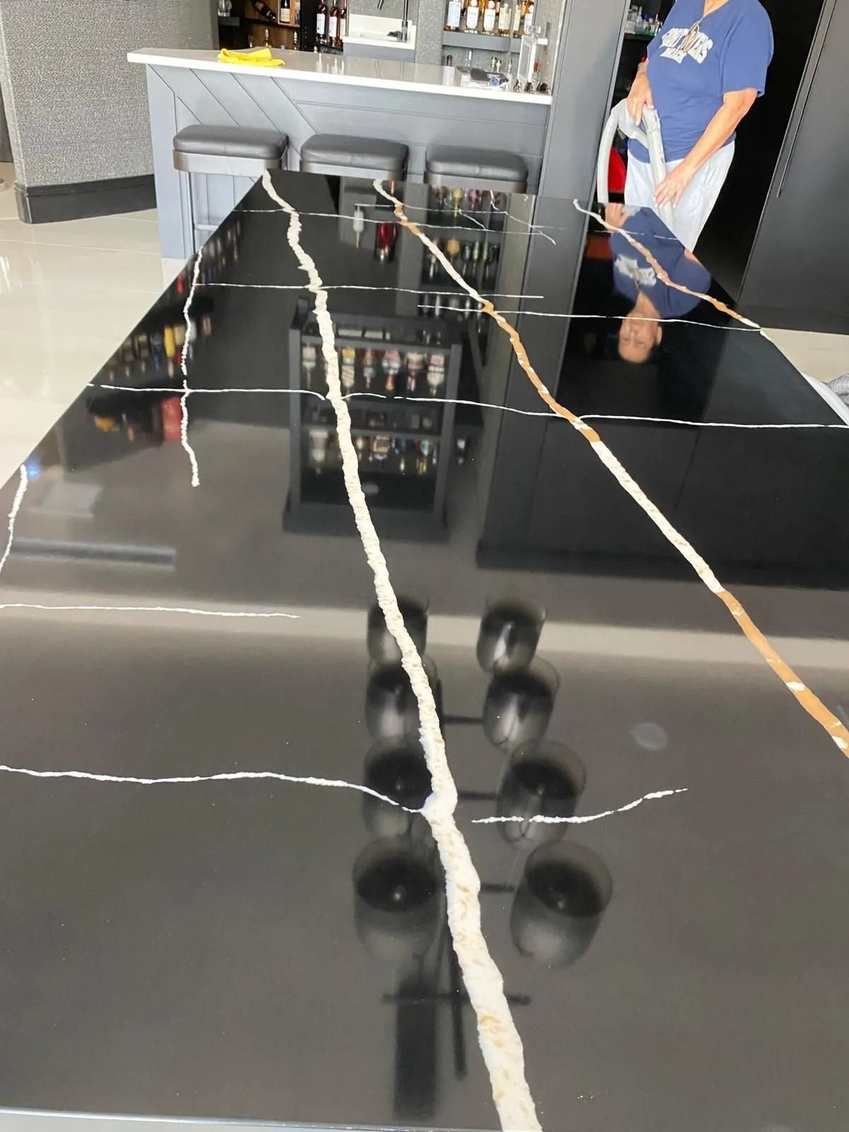 Black countertop with white/gold veining, reflecting bar scene and person.
