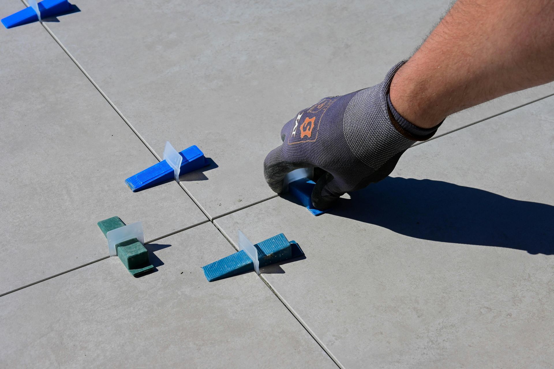 A gloved hand uses a blue tile leveling system on a concrete surface with tiled flooring.