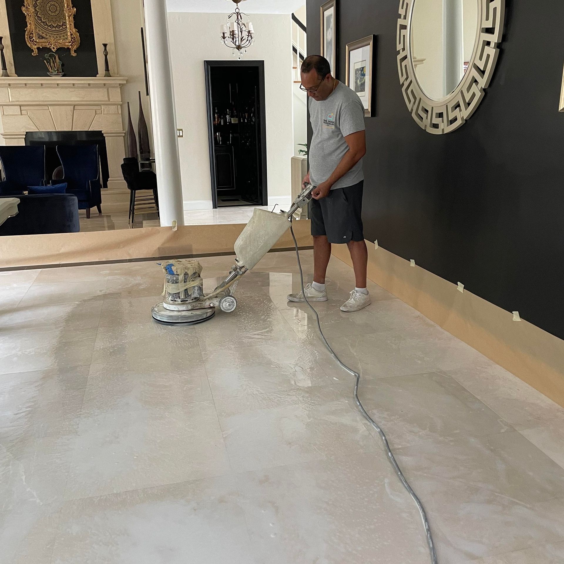 A man using a floor sander in a home. The floor is light, and the walls are dark.