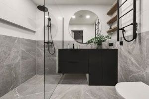 Modern bathroom with gray marble tile, black vanity, round mirror, and shower.