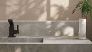 Bathroom vanity with matte black faucet, gray countertop, white vase with greenery, and beige textured wall.