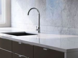 Modern kitchen sink with chrome faucet on white countertop and dark brown cabinets.