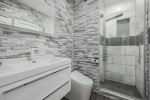 Modern gray and white bathroom with stone accent walls, a glass shower, and white vanity.