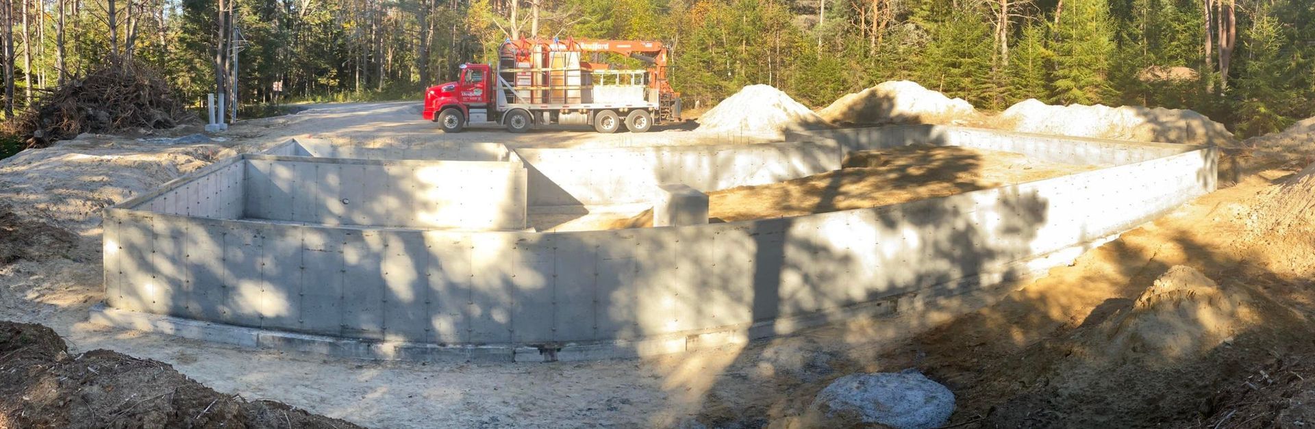 Un camion rouge roule sur un chemin de terre à côté d’un mur de béton.