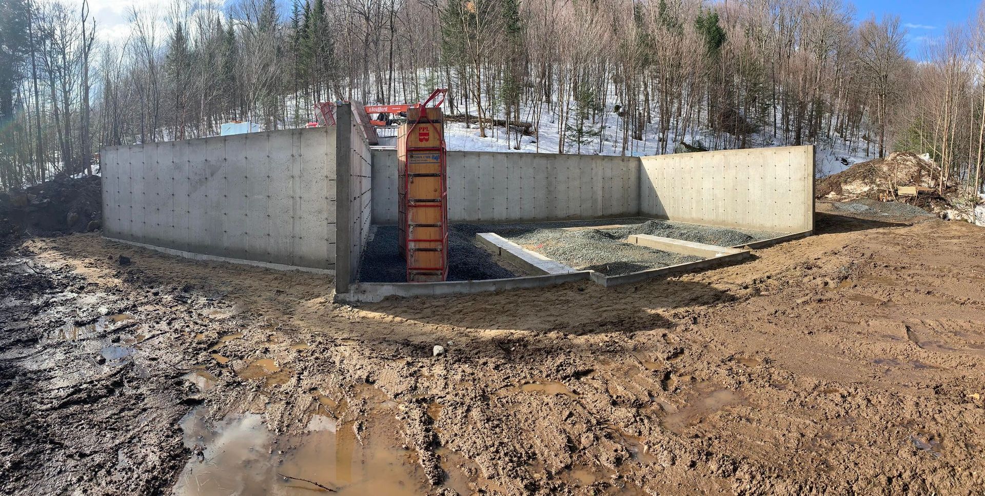 Un grand mur de béton est en train d'être construit au milieu d'un champ boueux.