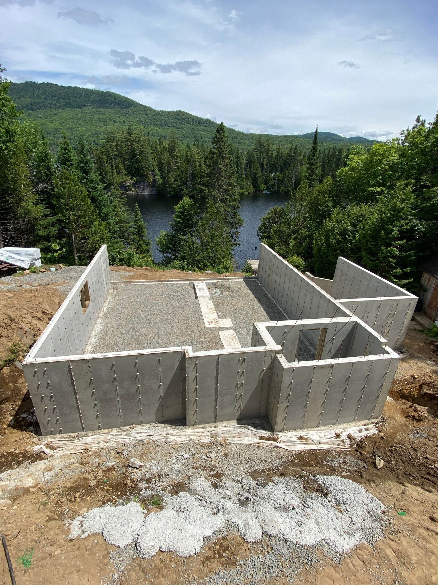 Une base en béton pour une maison est en cours de construction sur une colline surplombant un lac.
