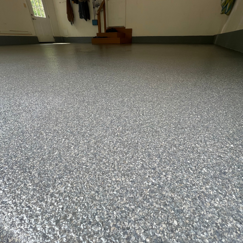 A close up of a gray floor in a garage with stairs in the background.