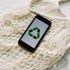 A cell phone with a recycling symbol on the screen is sitting on a white mesh bag.