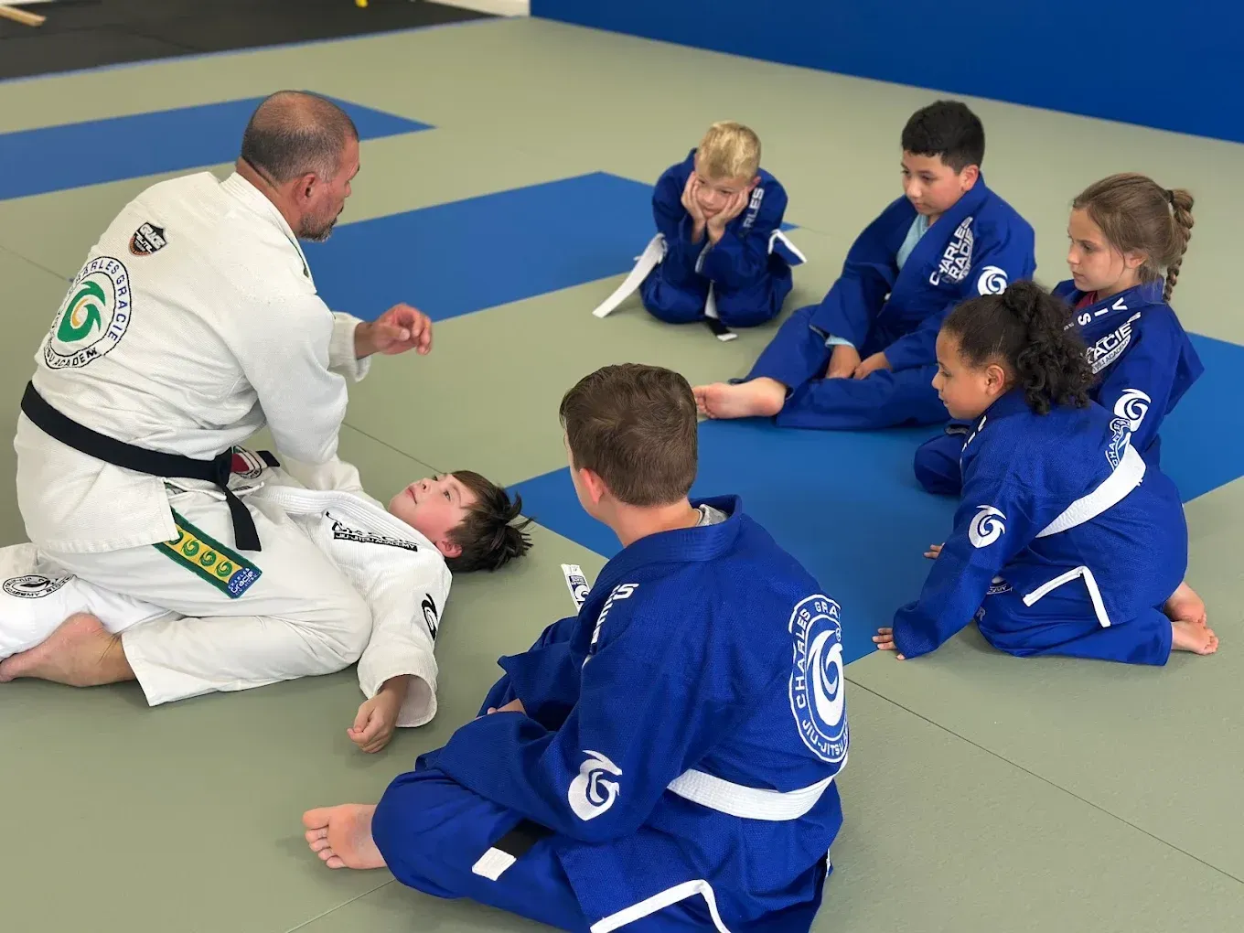 Instructor demonstrating technique to students in blue gis on mats.