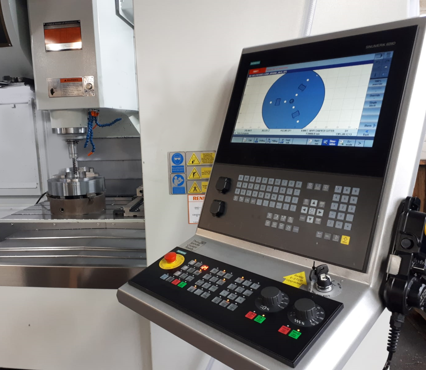 A CNC milling machine control panel with a screen showing a circular part diagram, positioned next to the machining area.