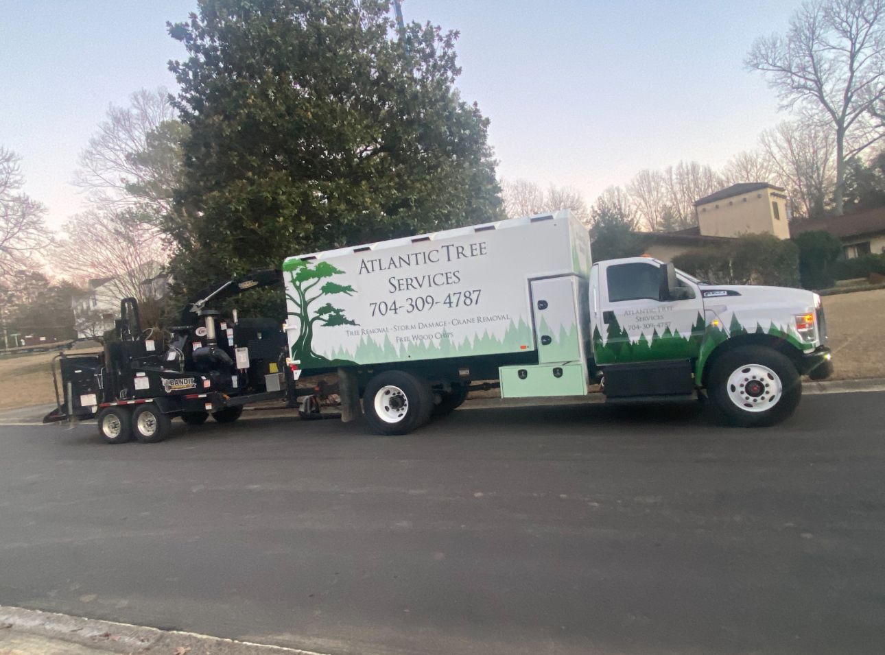 A white truck with a trailer attached to it is parked on the side of the road.