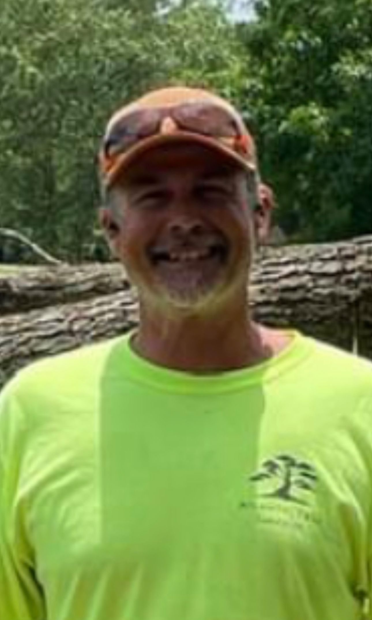 A man wearing a yellow shirt and an orange hat is smiling.