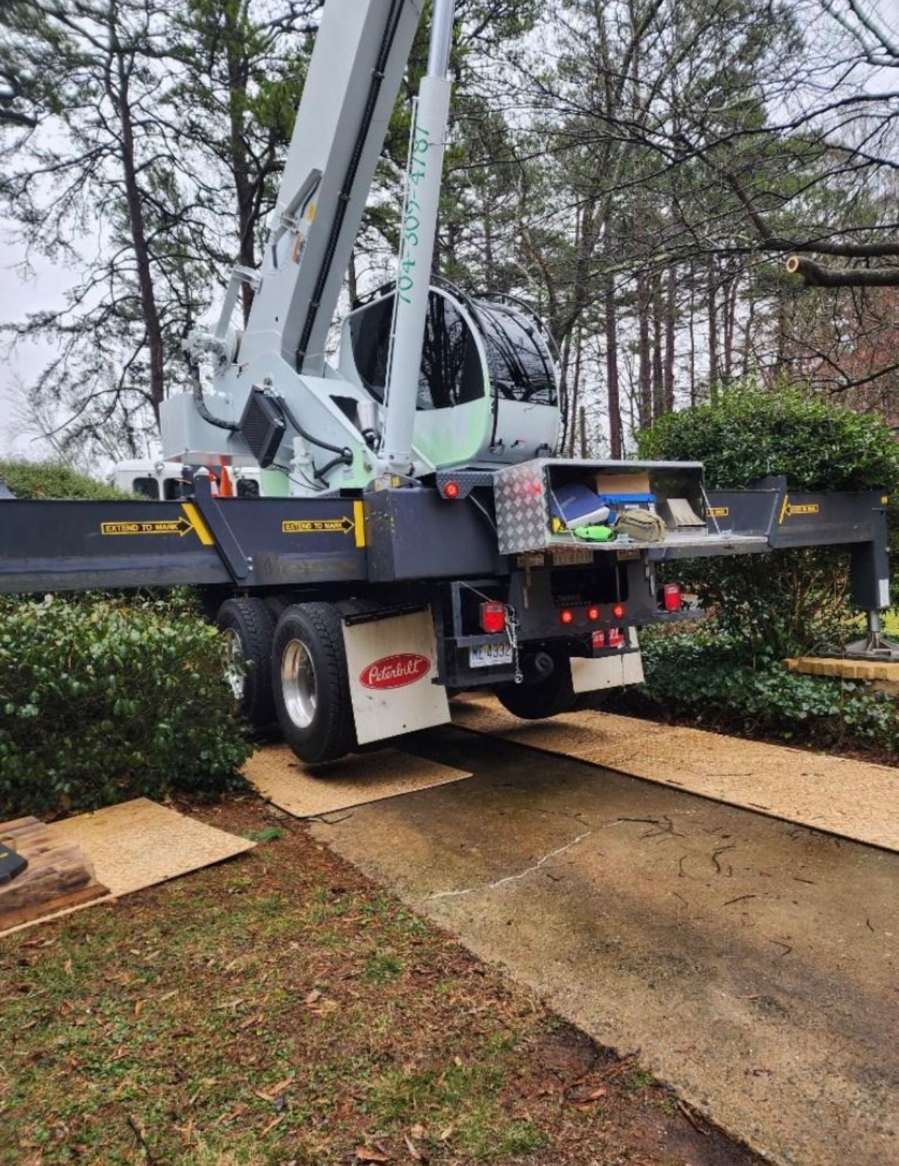 A large crane is parked in a driveway next to a tree.