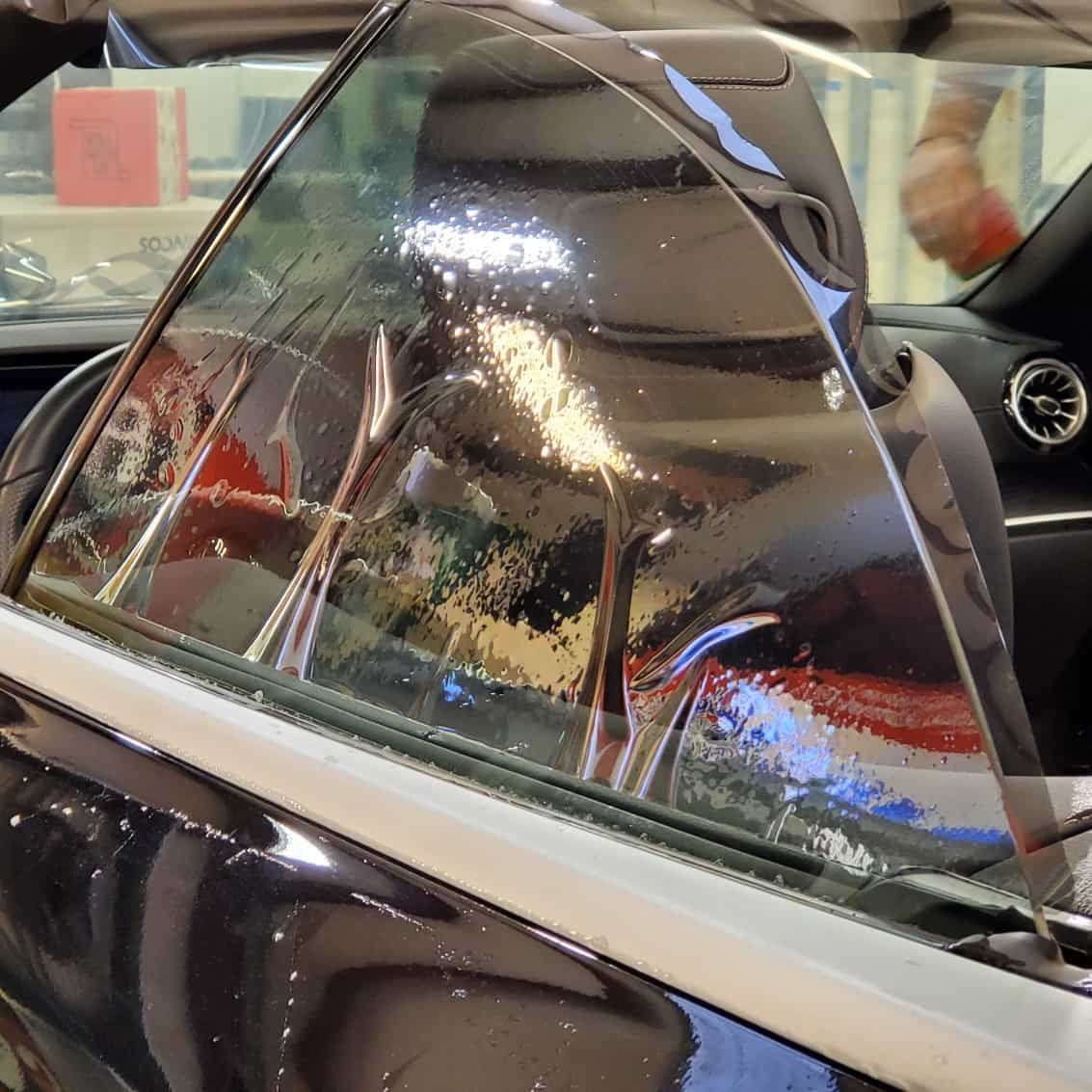 Car window with applied tint; reflective, wet appearance.