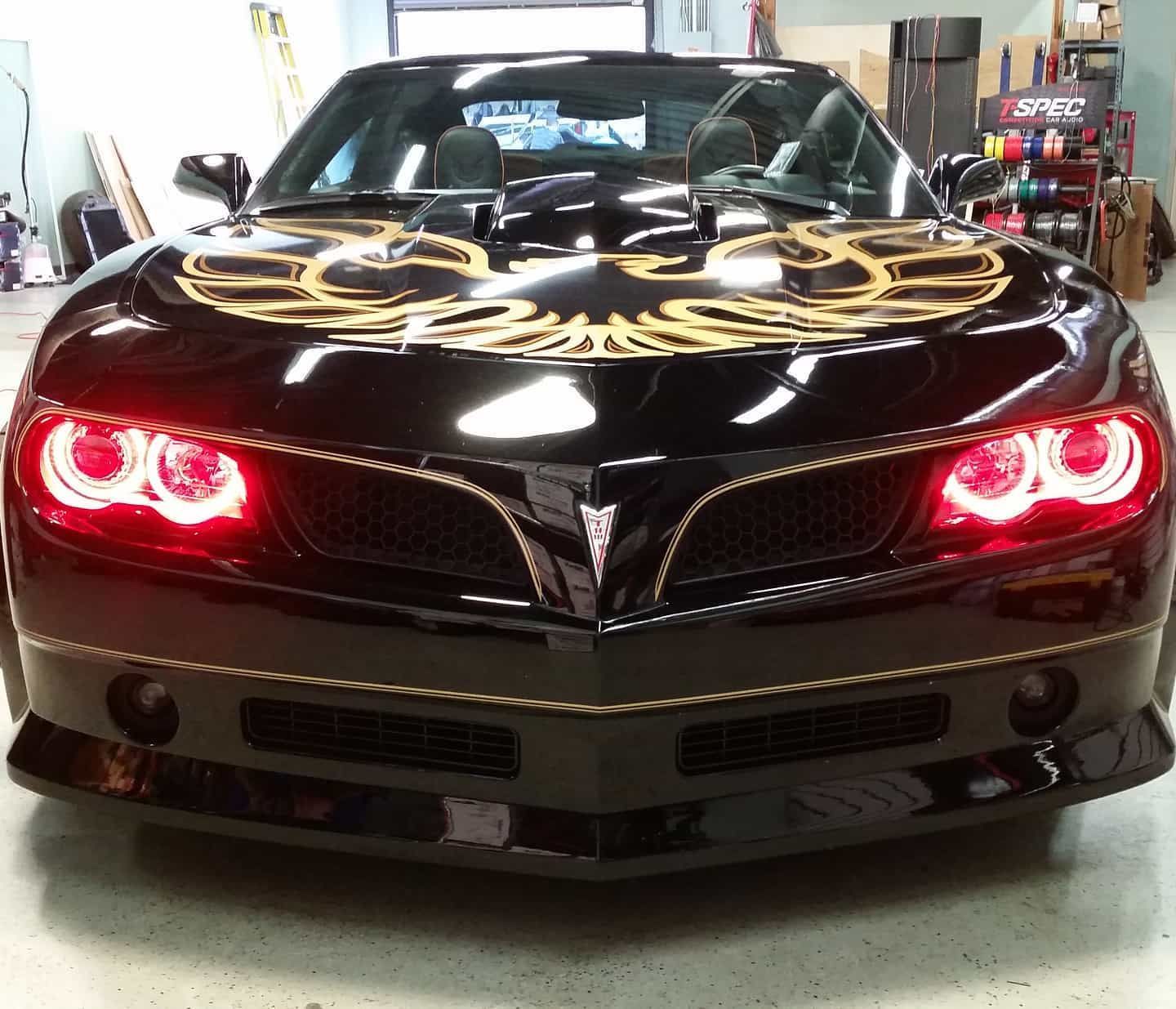 Black Pontiac Firebird with gold accents, glowing red headlights, in a shop.