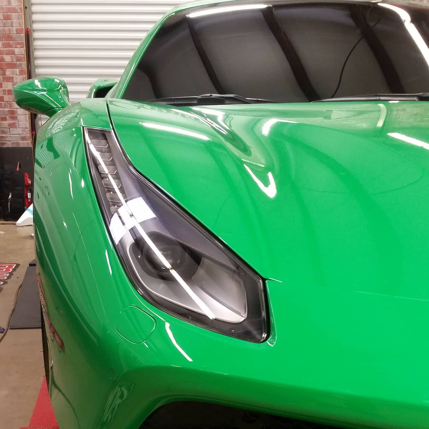 Green sports car's front with a black windshield, against a brick wall background.