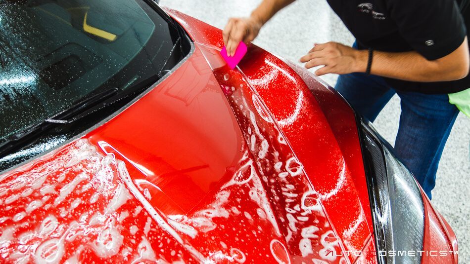 Person squeegeeing soapy red car hood.