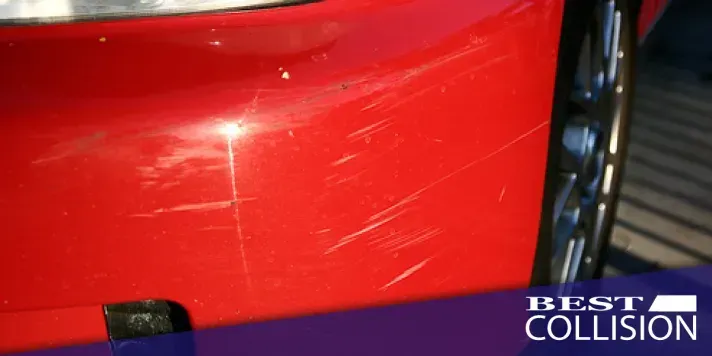 Red car bumper with scratches, a wheel is visible. 