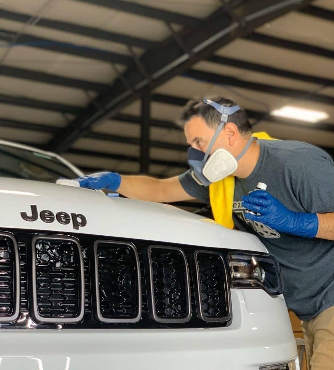 Man in mask and gloves applying product to the white hood of a Jeep.