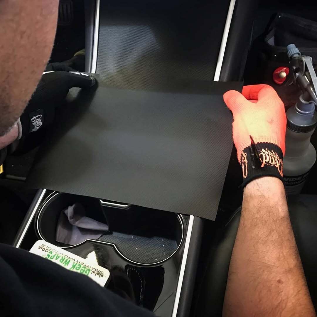 Person installing a black cover in a Tesla's center console; holding it with gloved hands.