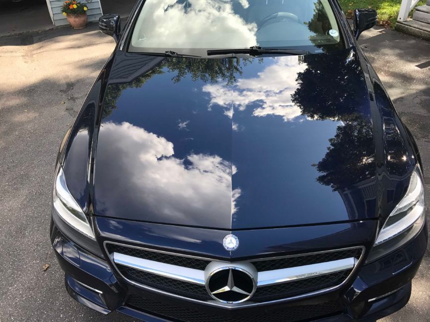 Dark blue Mercedes-Benz car hood reflecting a cloudy sky, parked outside on a sunny day.