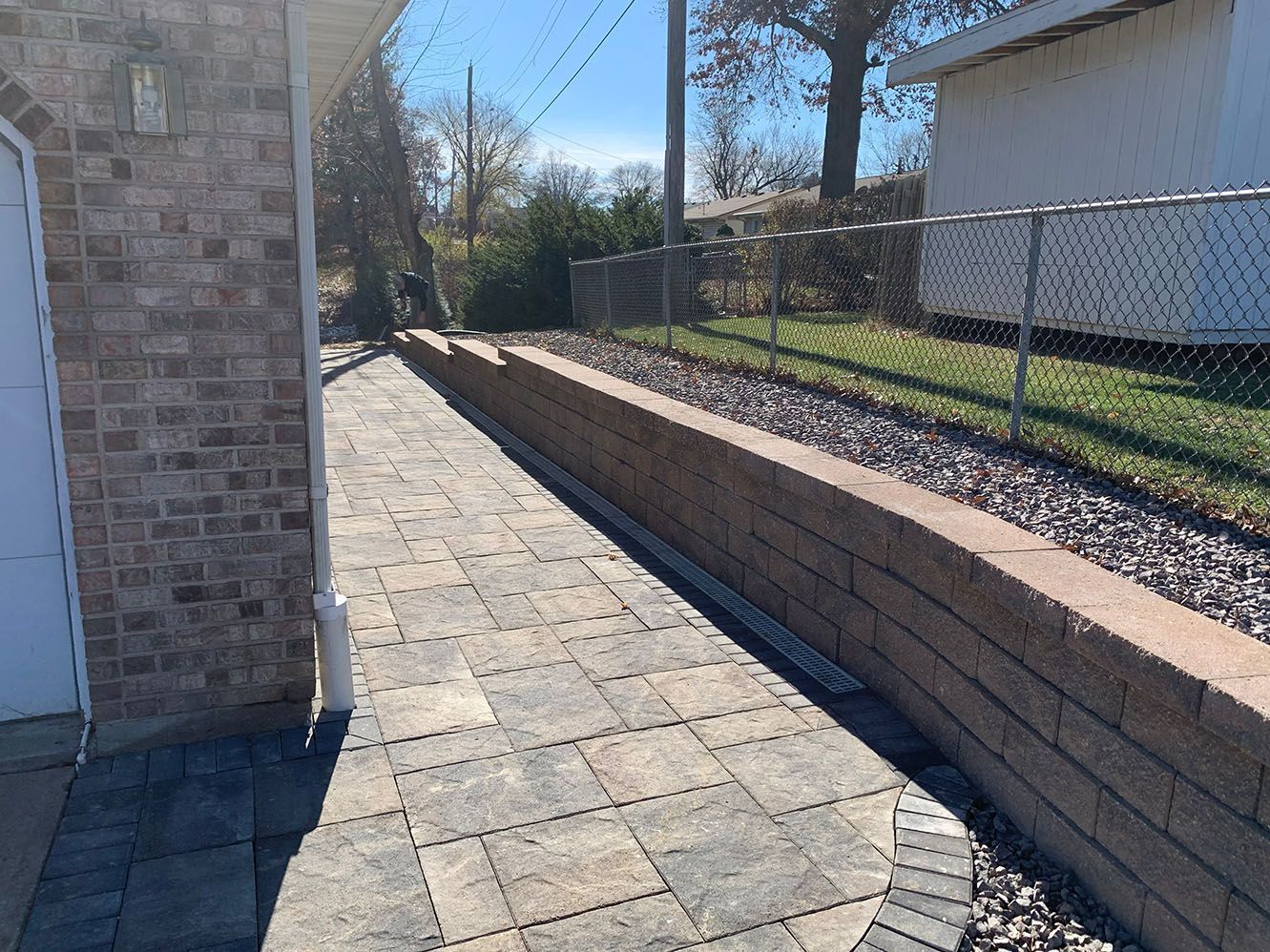 A brick walkway bordered by a stacked stone retaining wall next to the side of a brick house.