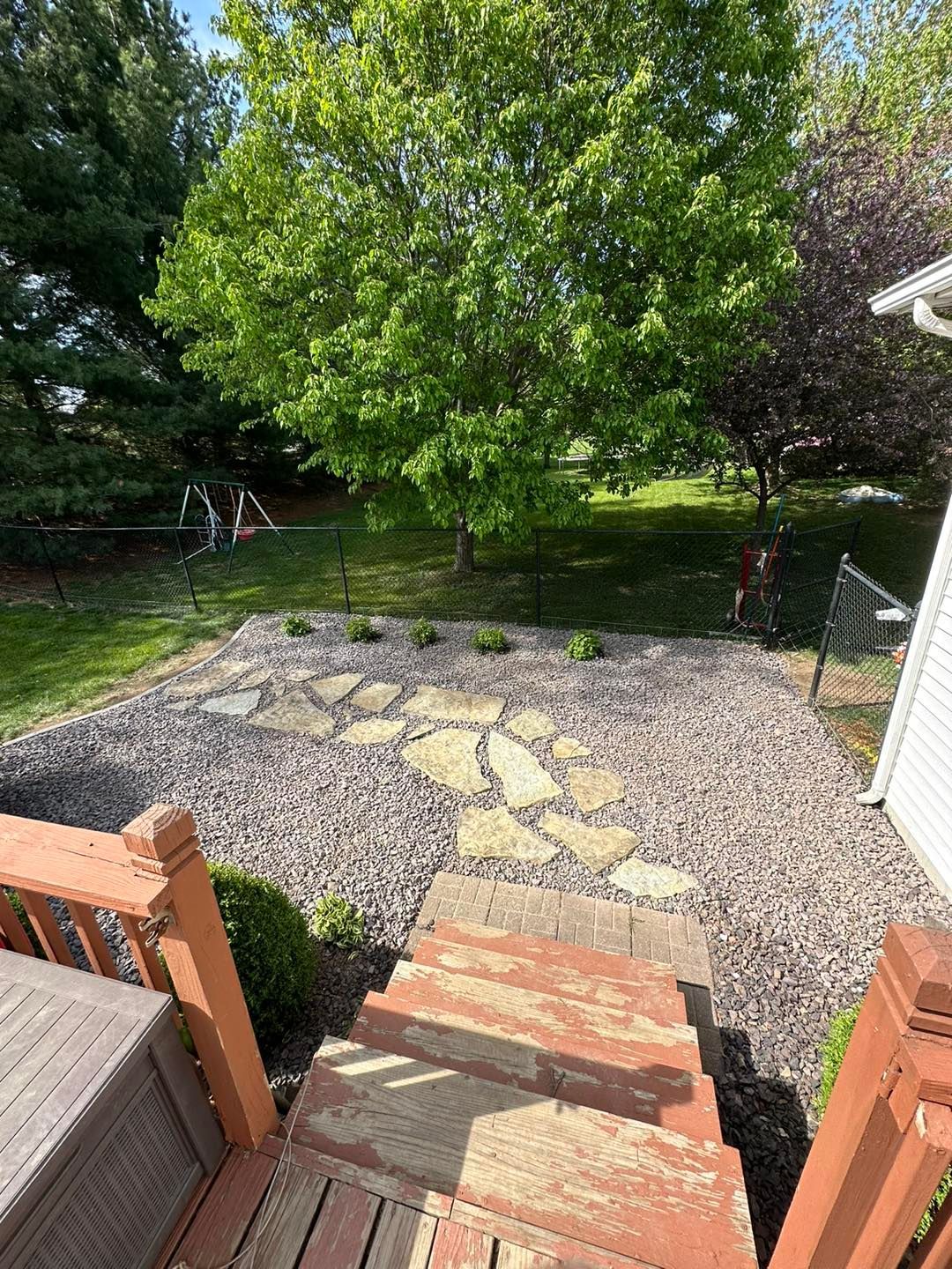 A view from a wooden deck looking down stone steps into a backyard featuring a gravel patio with a natural stone path.