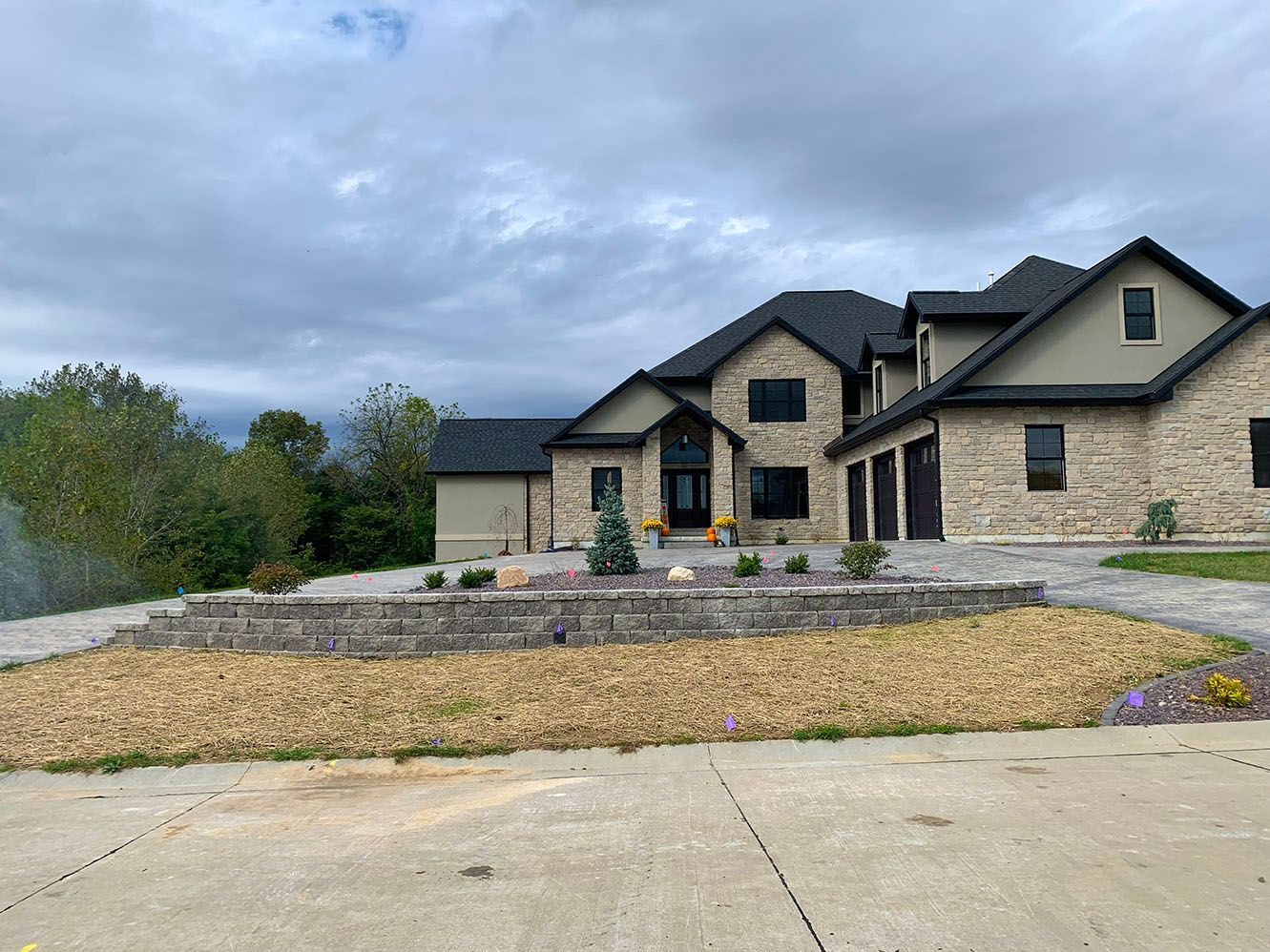 A large stone and tan-sided house with a dark roof and a multi-tiered stone retaining wall in the front yard.