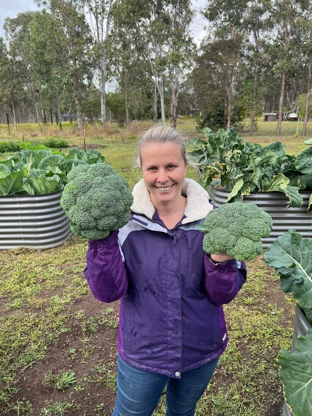 A woman in a purple jacket is holding two broccoli heads in her hands.