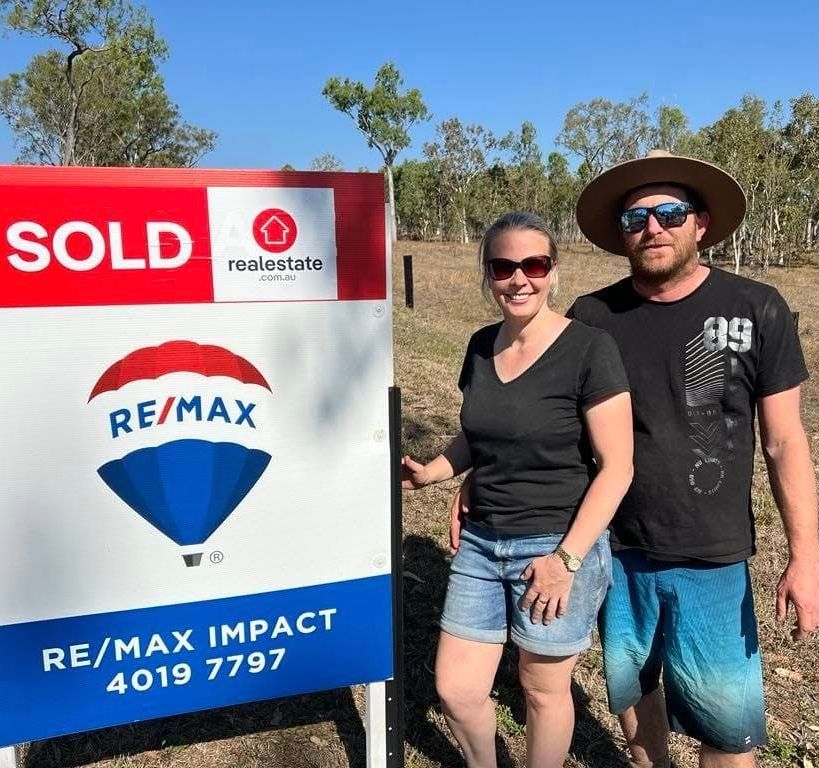 A man and woman standing in front of a sold sign