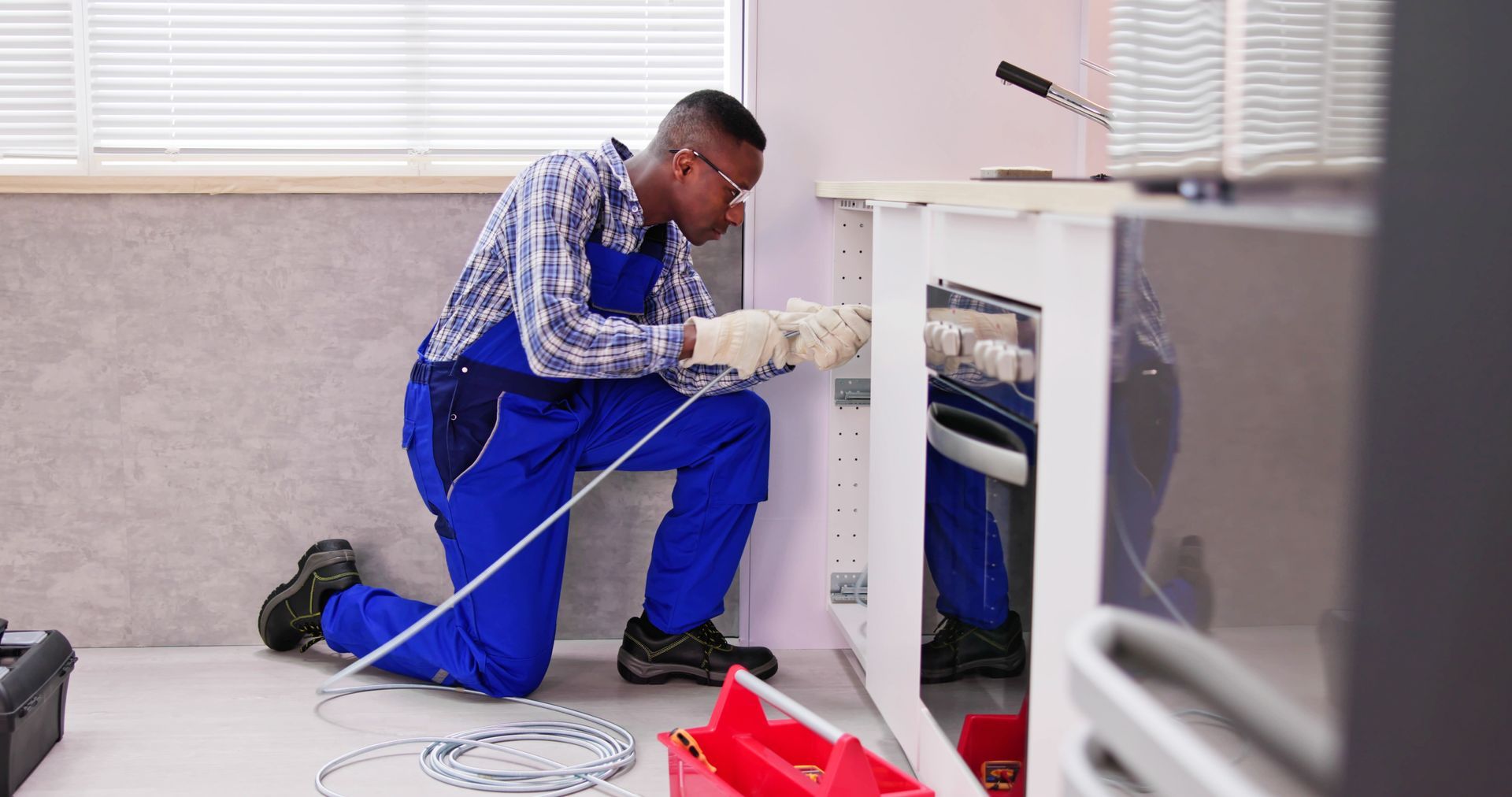 A man is kneeling down in a kitchen fixing a sink.