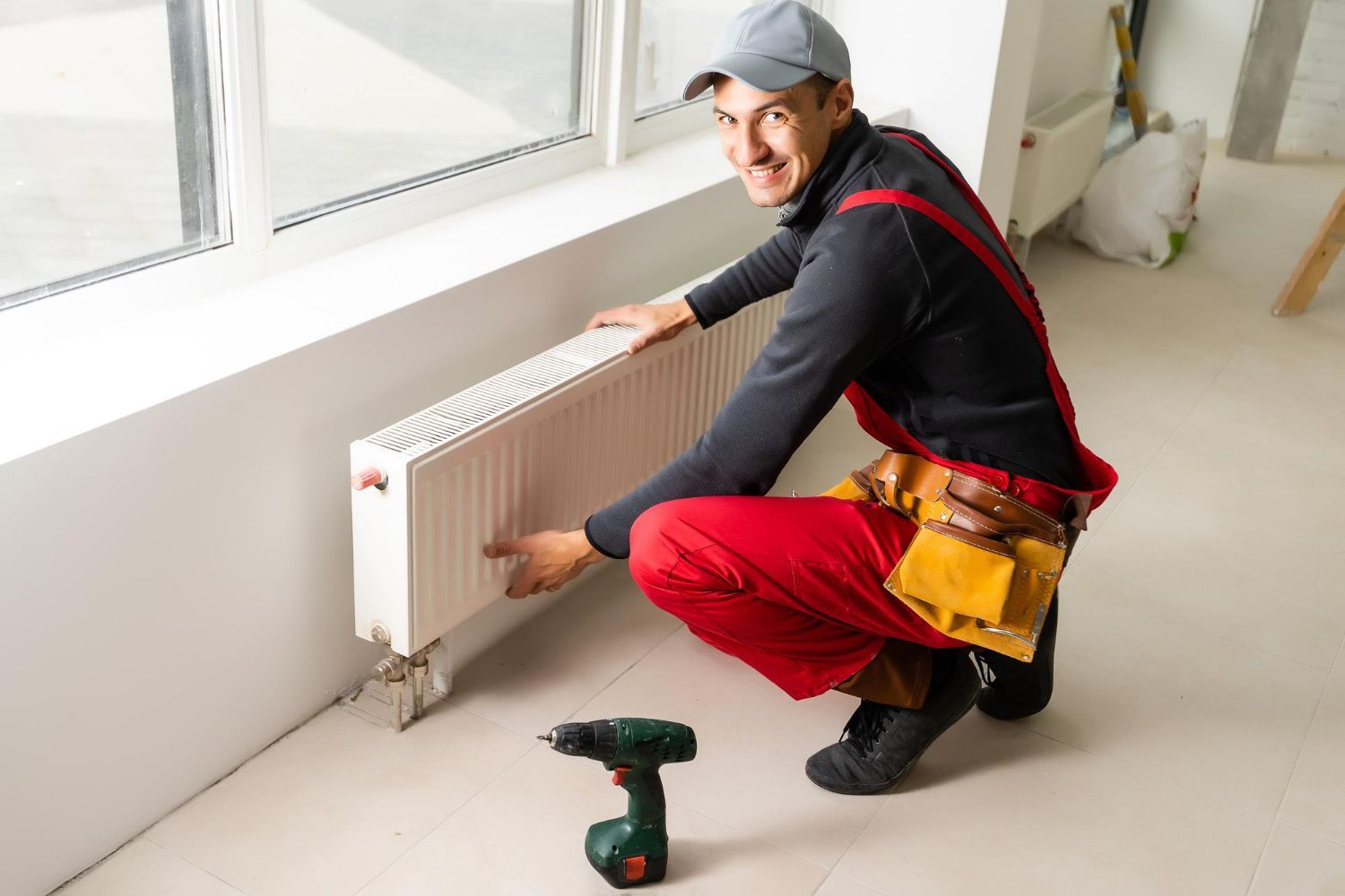 A man is installing a radiator in a room next to a window.