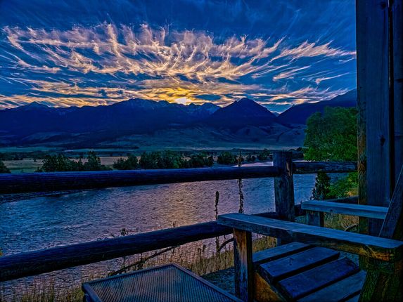 A chair is sitting on a balcony overlooking a lake at sunset.