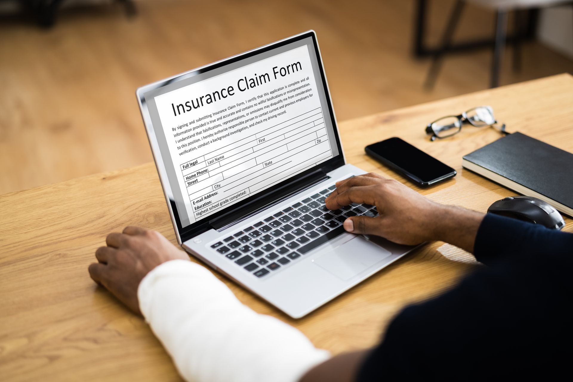 Person with bandaged arm showcasing workers compensation claim, filling out online insurance form. Person with bandaged arm showcasing workers compensation claim, filling out online insurance form.