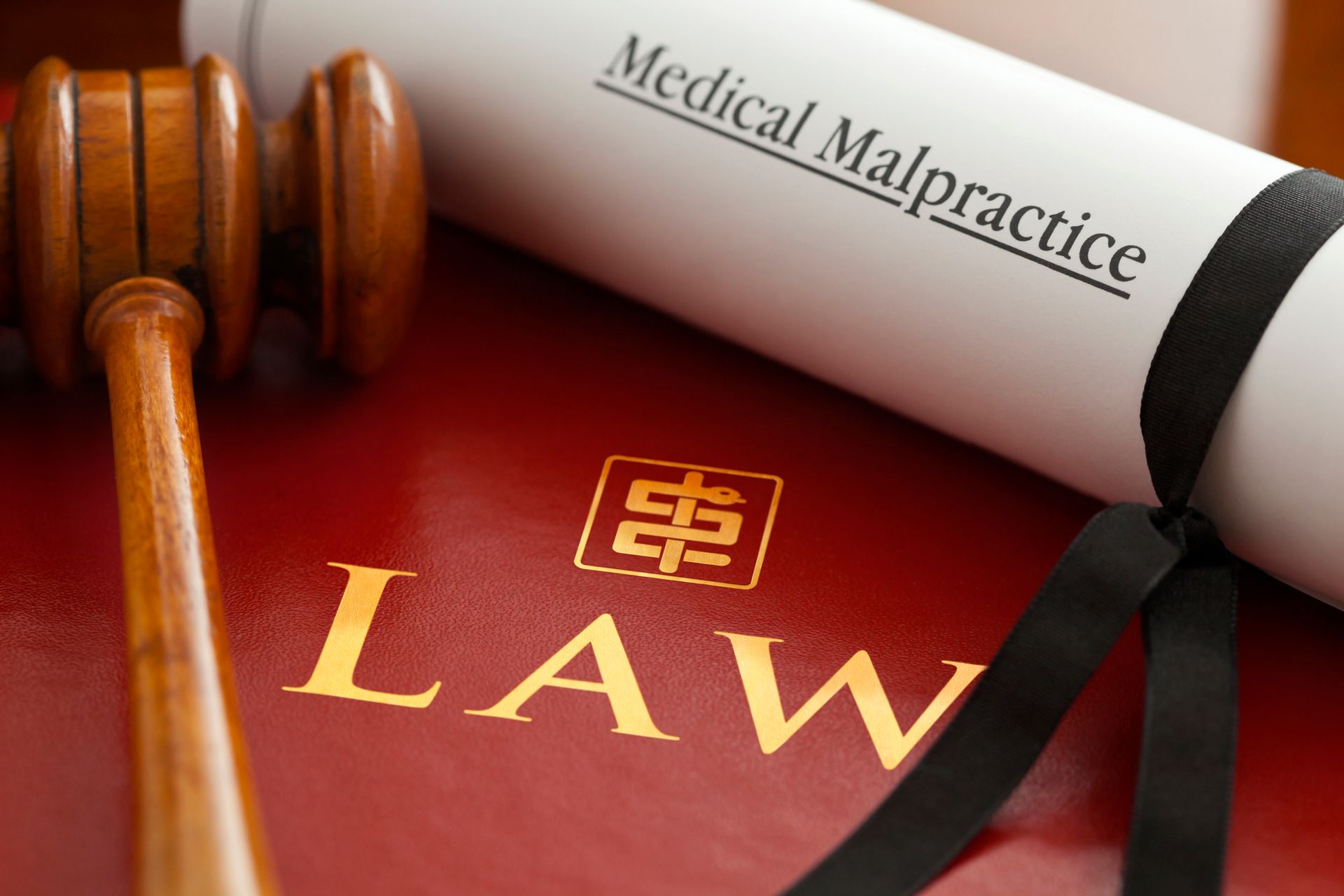 Red leather medical law book with gold Law word, stylized logo, a judge’s gavel and a document.