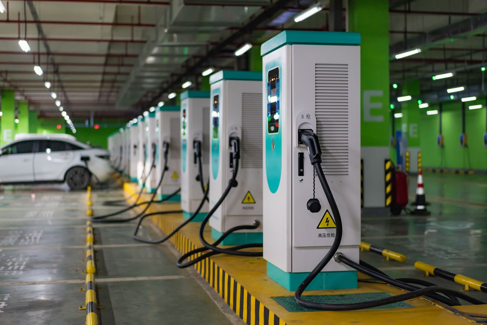 A white car is being charged at a charging station in a parking garage.