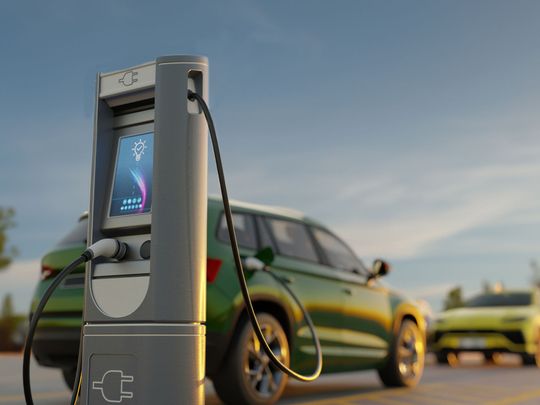 A green electric car is being charged at a charging station.