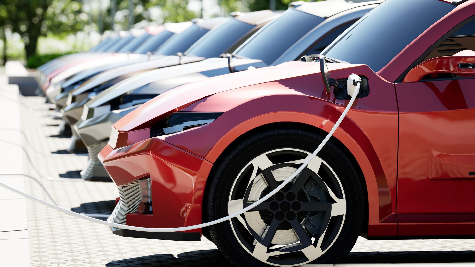 A row of electric cars are charging in a parking lot.